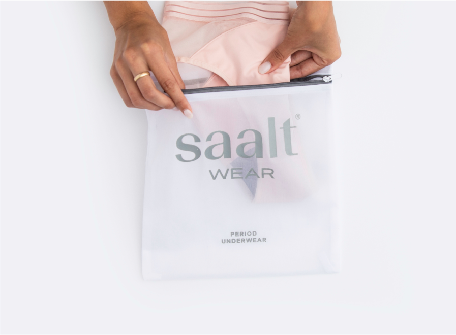 Image showing how to wash period underwear safely - place them in a mesh bag. Models hands shown placing pink Mesh Hipster Saalt Wear period-proof and pee-proof underwear being placed in a Saalt Wear Period Underwear Mesh Bag.