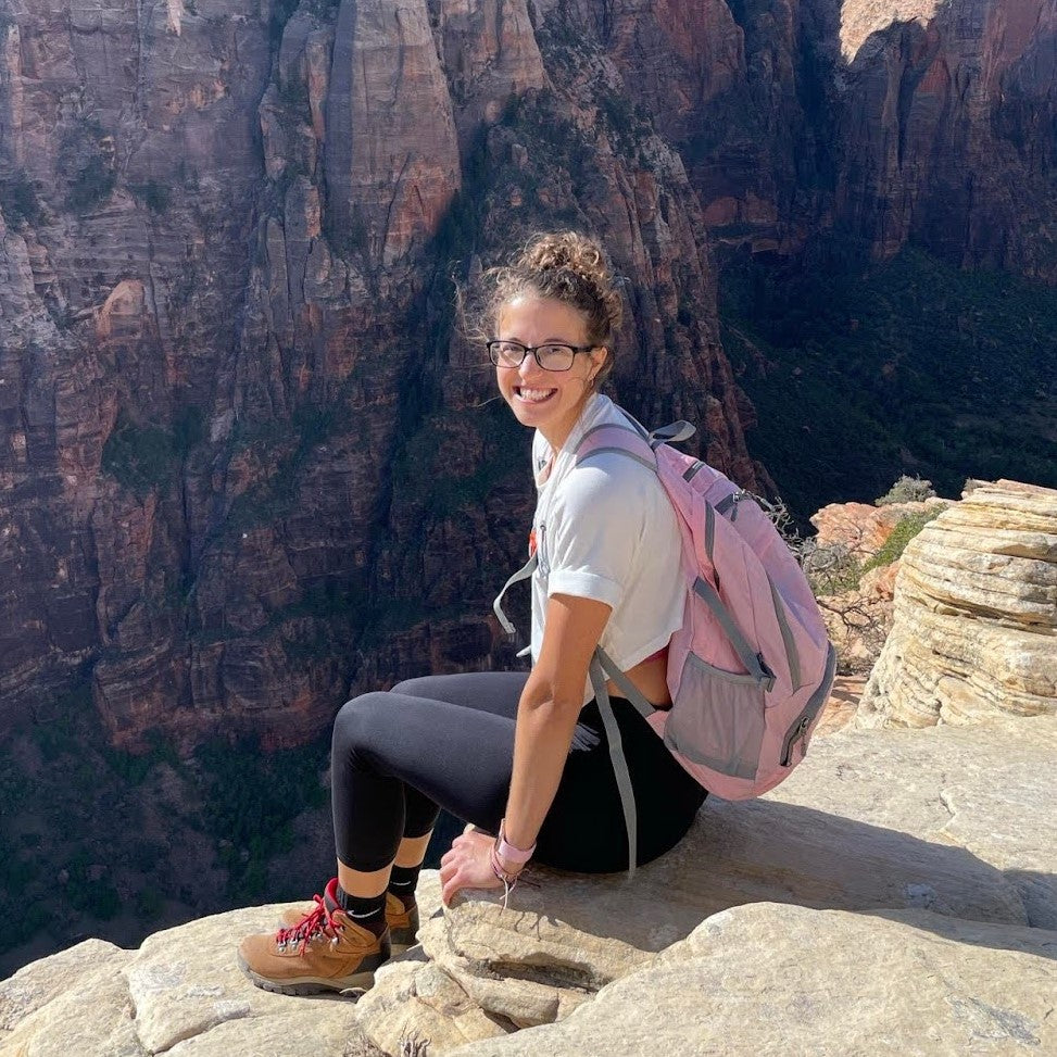 Image of Dava sitting on the edge of a canyon, wearing a backpack and hiking boots.