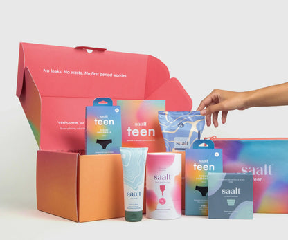 Colorful period product packaging with "saalt teen" branding in an open box. A hand reaches for a pouch of Saalt Wipes. Text inside box says, "No leaks. No waste. No first period worries."